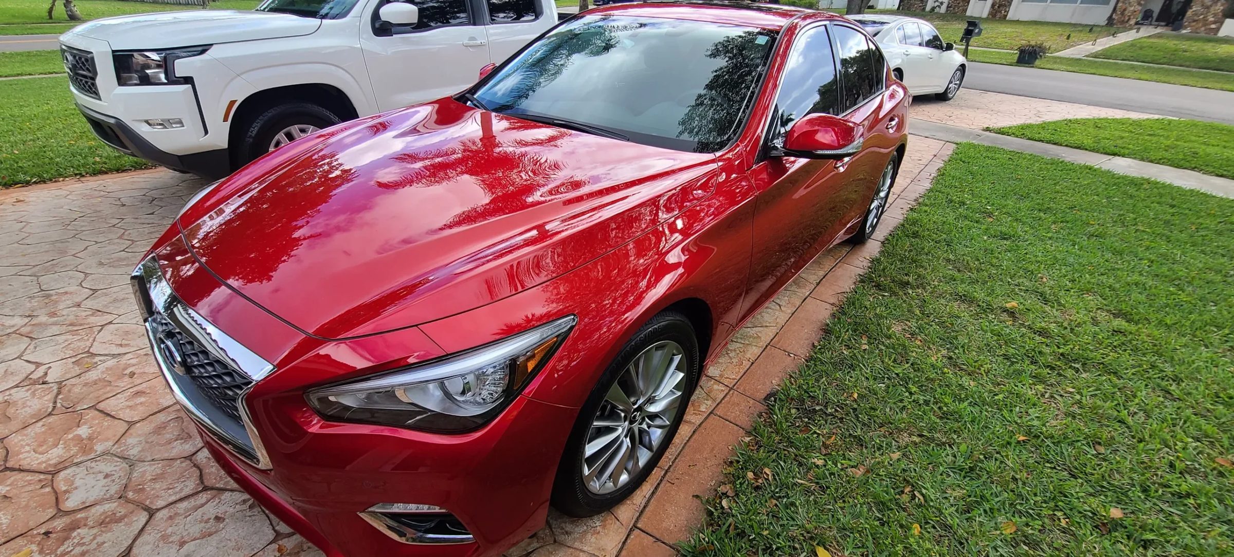 Freshly detailed red Infiniti Q50 sedan gleaming on a red paver driveway outside a South Florida home